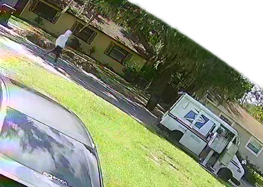 A security camera still of a person in a hoodie walking toward a parked mail truck.
